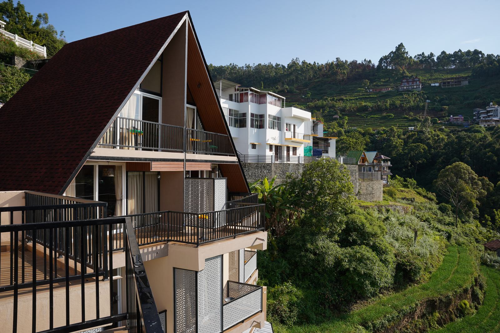 Alpine Cabin's steep timber A-frame roofline in daylight, with the Calanthe building and terraced hills behind it.