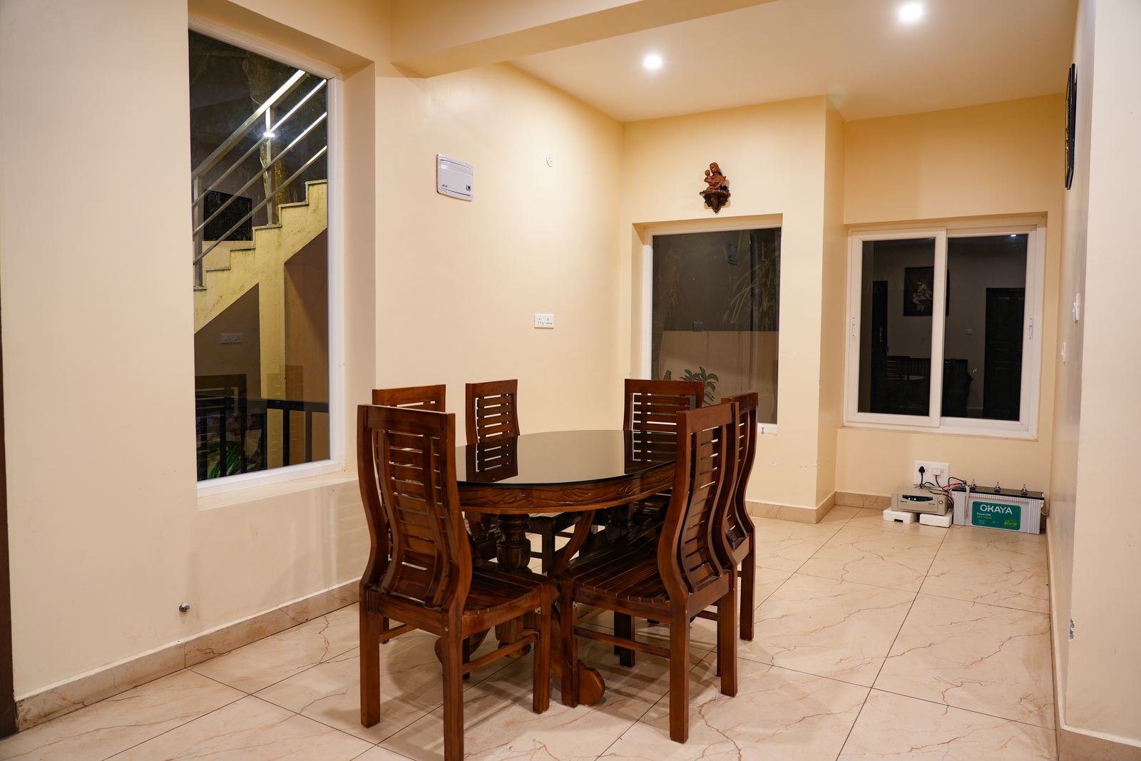 The dining room set for a meal, a dark wood table and carved chairs beneath a stairwell landing.
