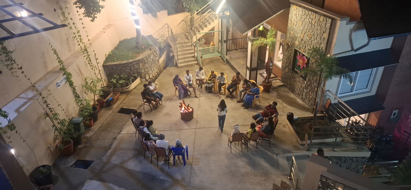 Guests seated in a circle around a lit firepit in the courtyard at night, the property's stone and timber buildings glowing around them.