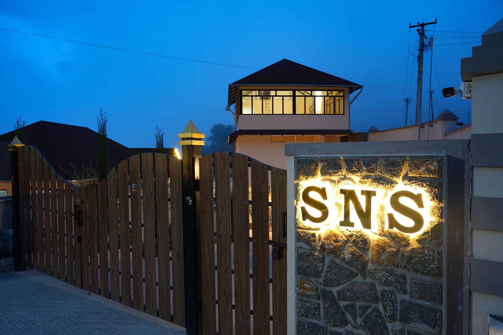 The property's stone entrance gate lit up at night, with the SNS name built into the pillar beside it.