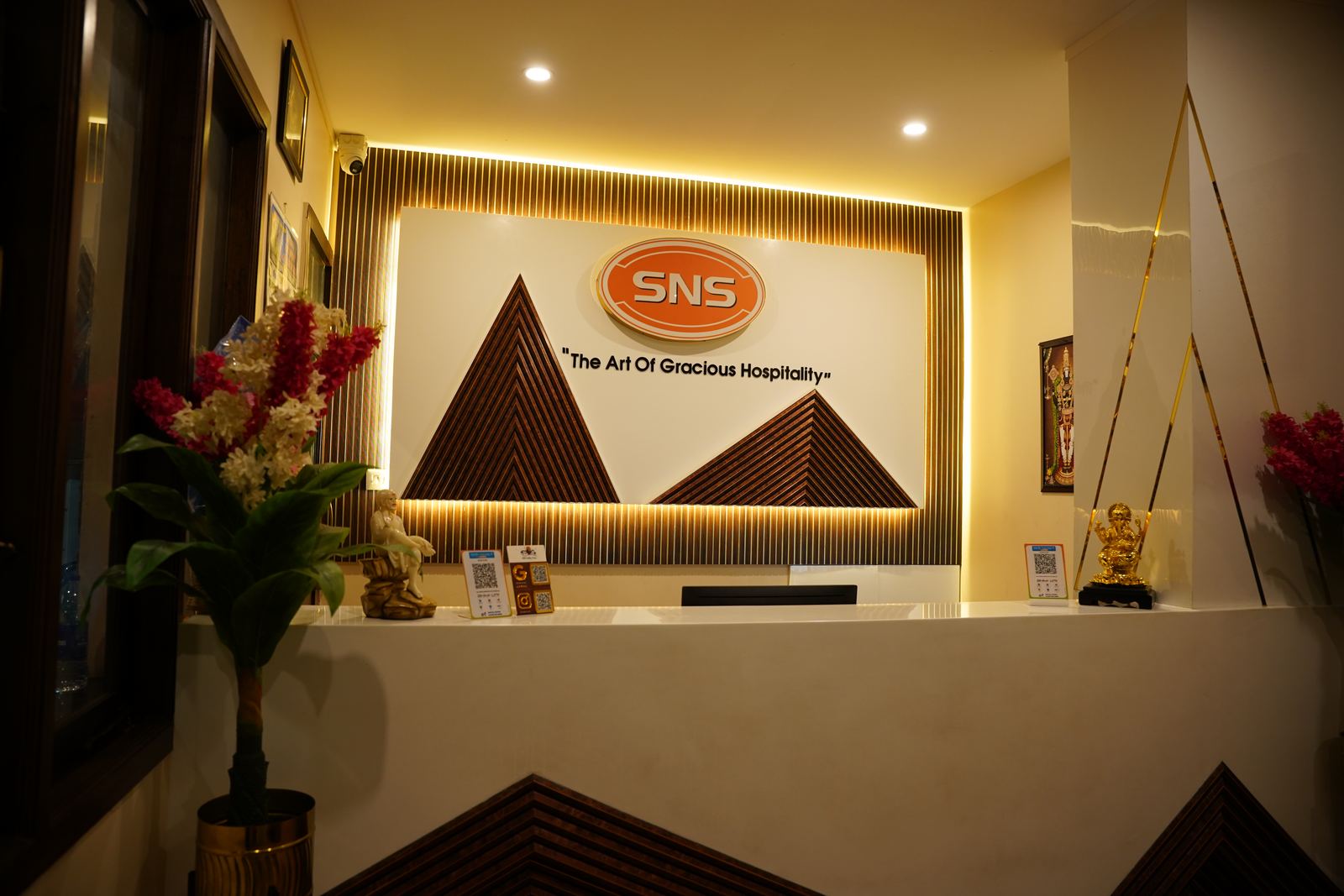 The reception desk, backlit with the SNS wordmark and the line "The Art of Gracious Hospitality" above it.