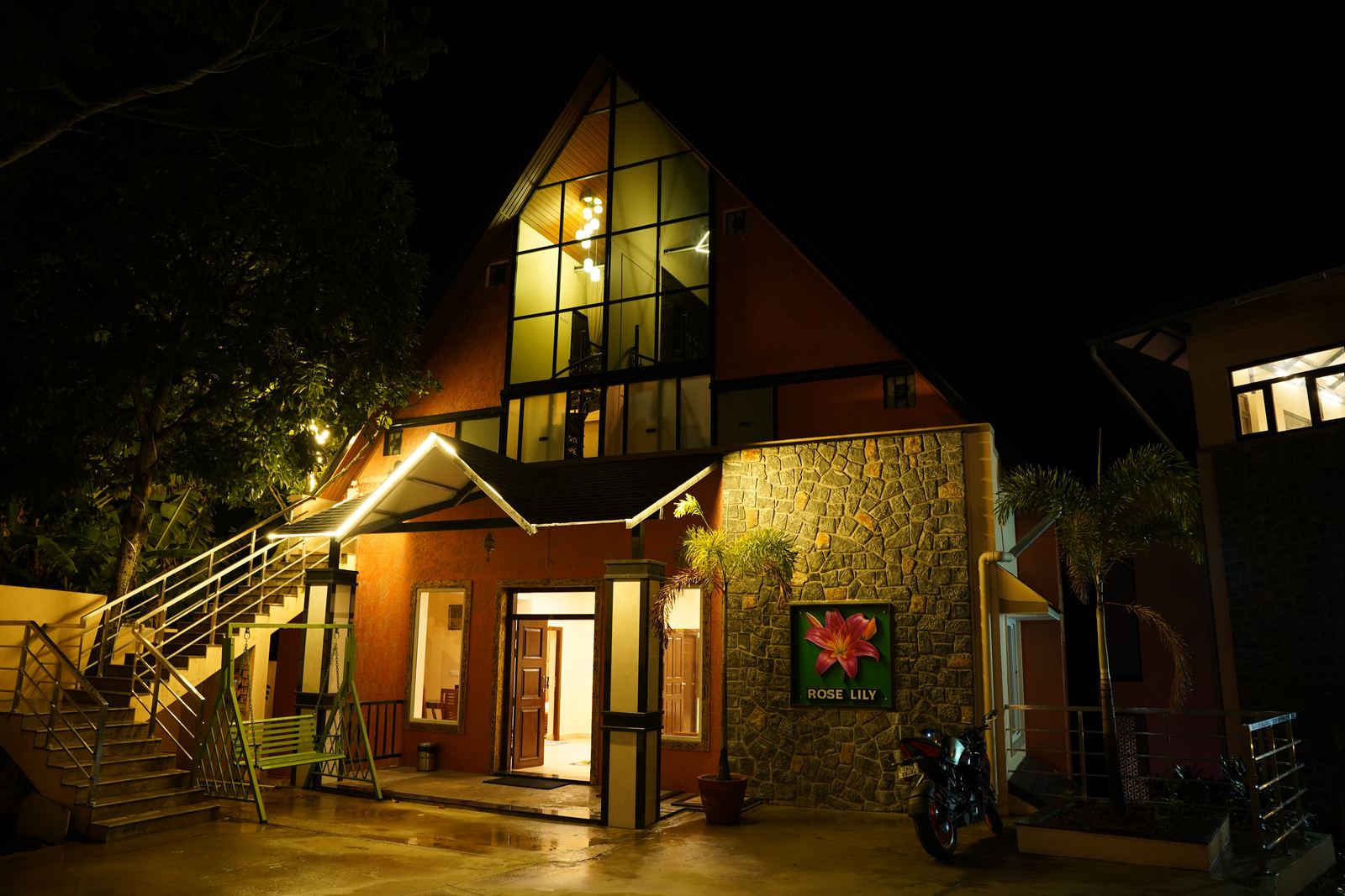 The Rose Lily building's stone-and-timber facade lit up at night, its tall arched window glowing from within.