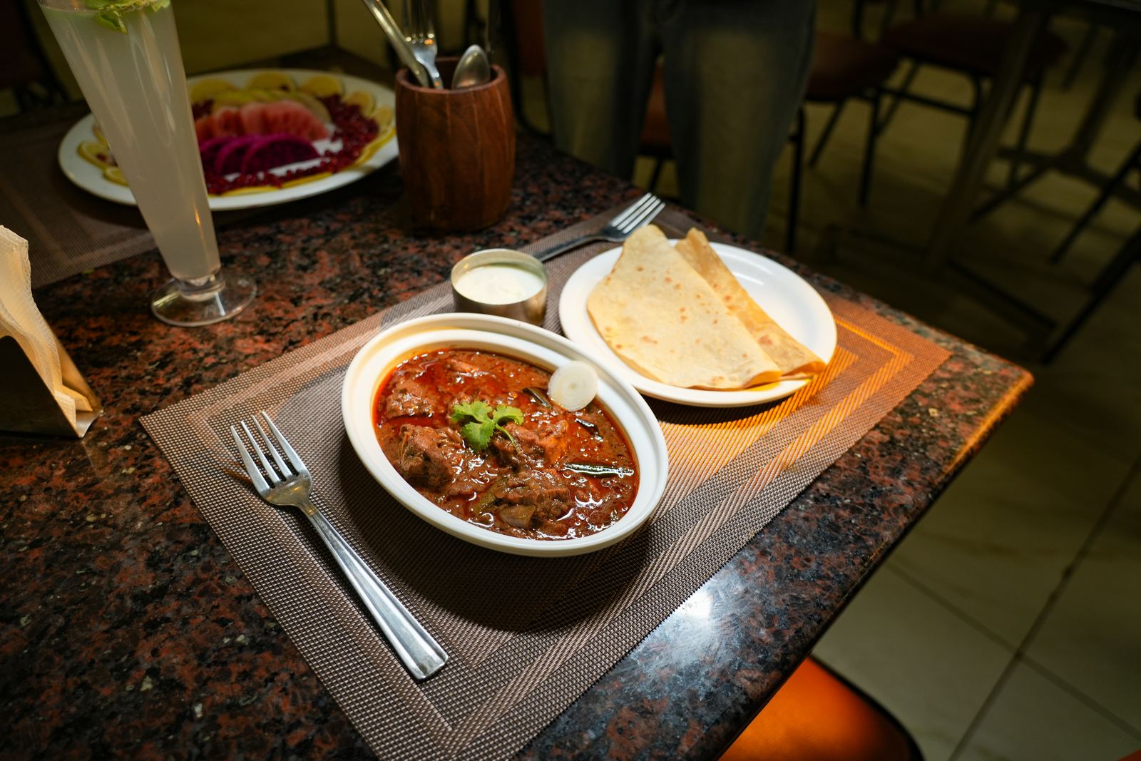 A second bowl of spiced meat curry with parathas, photographed table-side