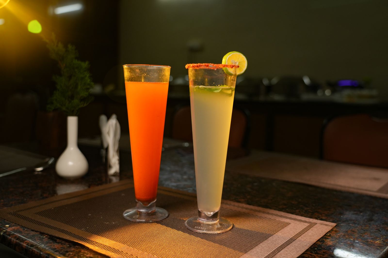 Two tall glasses of mocktails, one orange and one lime with a spiced rim