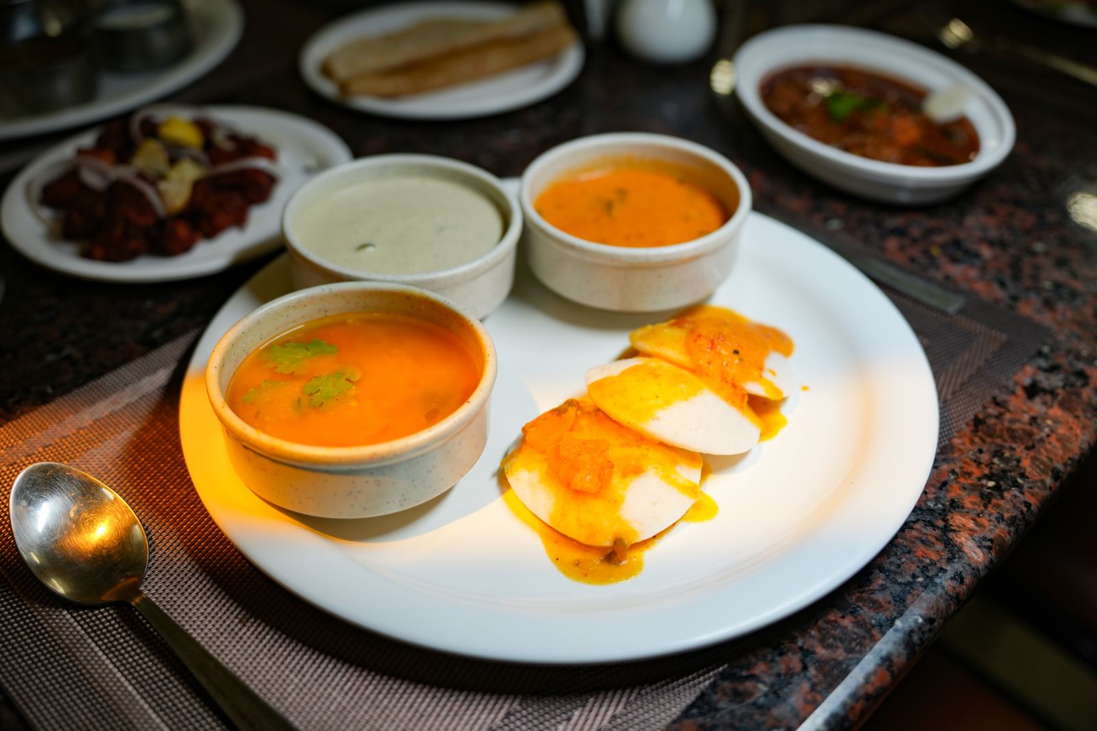 Three bowls of soup served alongside a sliced steamed dish in a spiced sauce